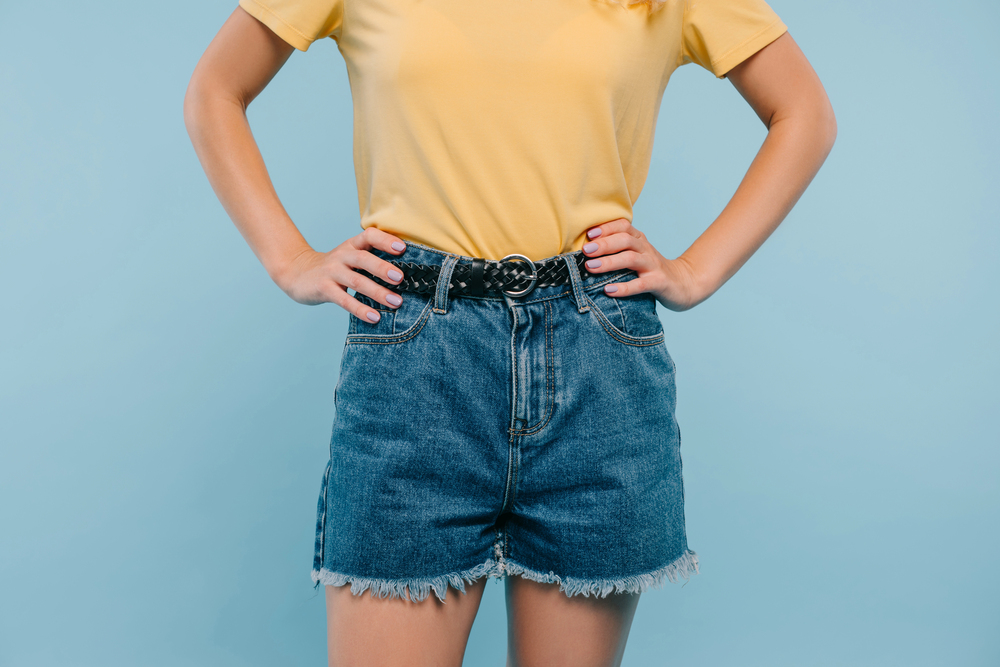 Bijgesneden afbeelding van meid met geel shirt en korte broek voor blauwe achtergrond